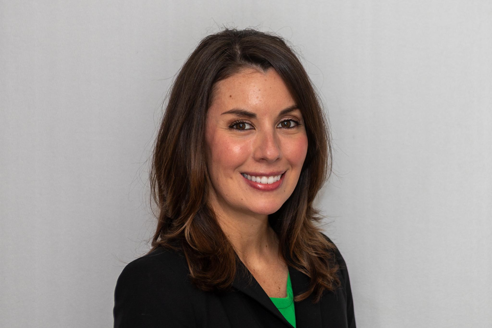 Smiling woman in a black jacket against a light gray backdrop